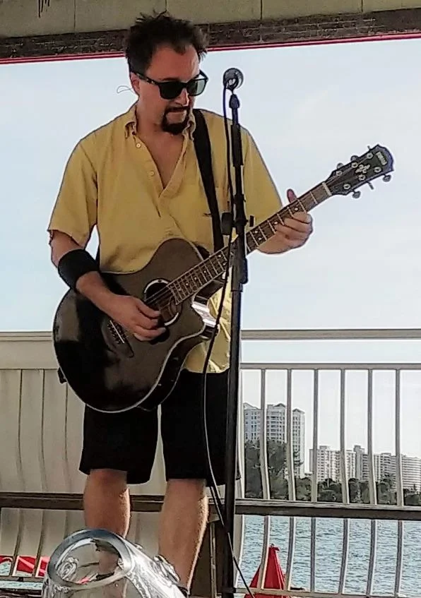 Musician performing live with an acoustic guitar by the waterfront