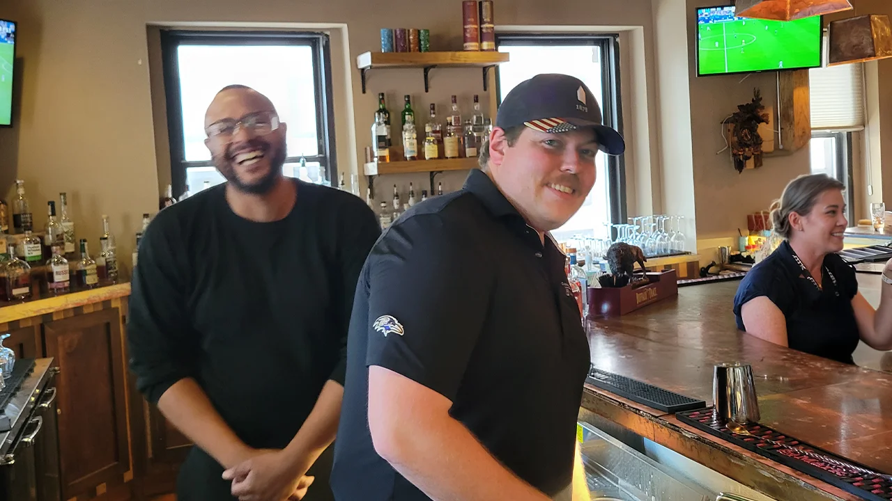 Bartenders smiling and mixing drinks at a lively bar