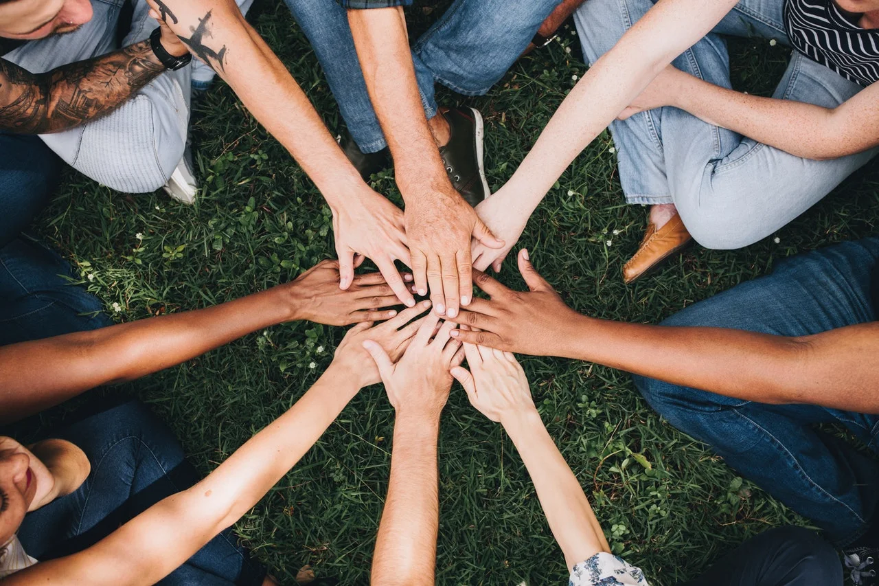 Diverse hands gathered in a circle on grass, symbolizing unity and collaboration.