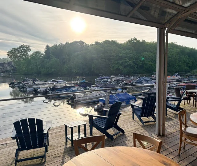 Two blue Adirondack chairs and a small table overlooking a marina.