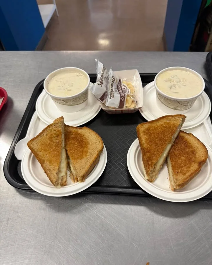 A tray with grilled cheese sandwiches, two cups of clam chowder, and a small dessert.