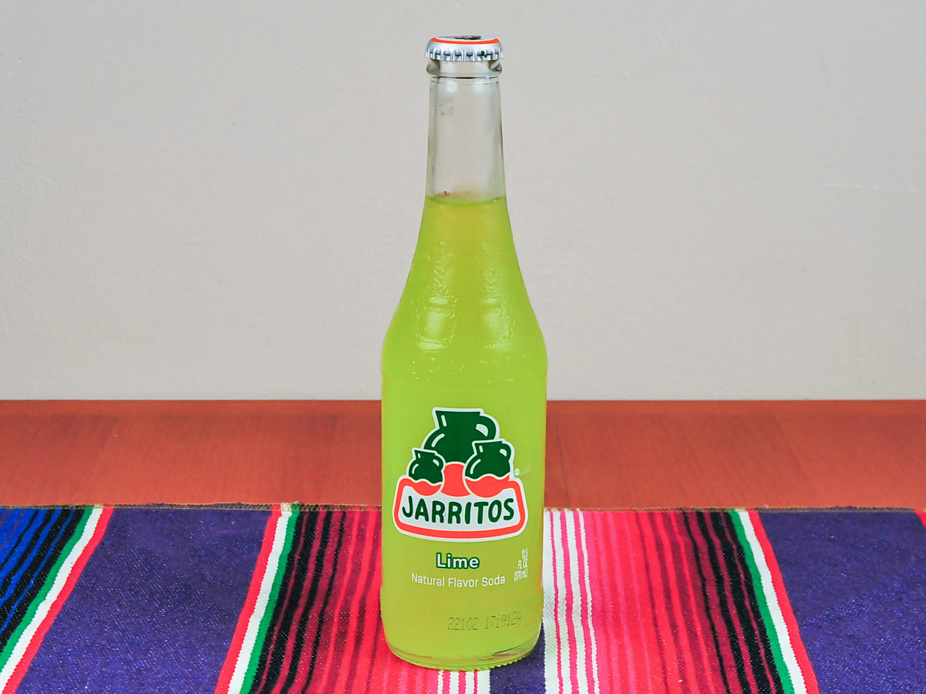 A bright green bottle of lime soda, showcased on a colorful striped background.