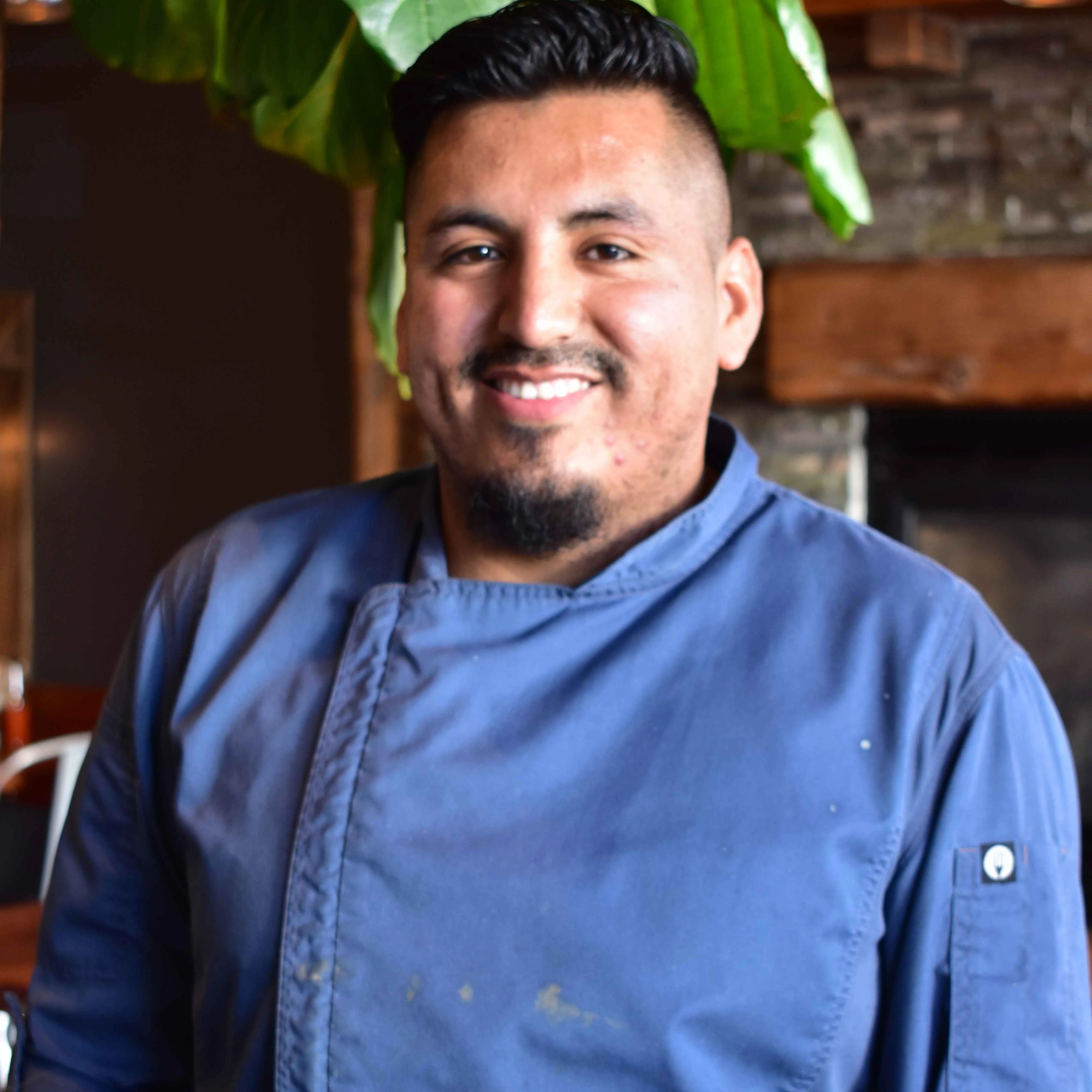 Chef smiling in a cozy restaurant setting with greenery