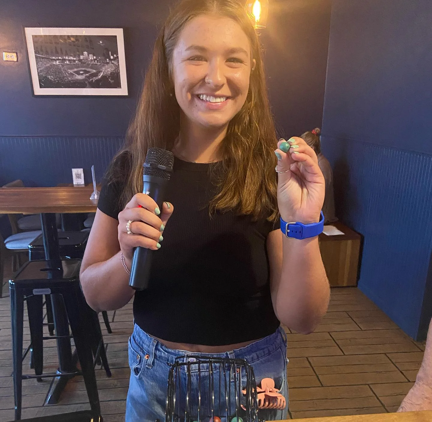 Hostess holding bingo balls and microphone in a lively bar setting