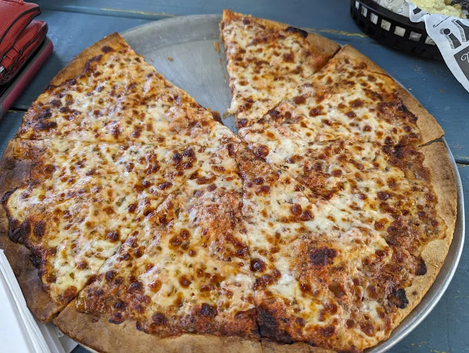 A large pizza with melted cheese and a few slices missing, served on a metal tray.