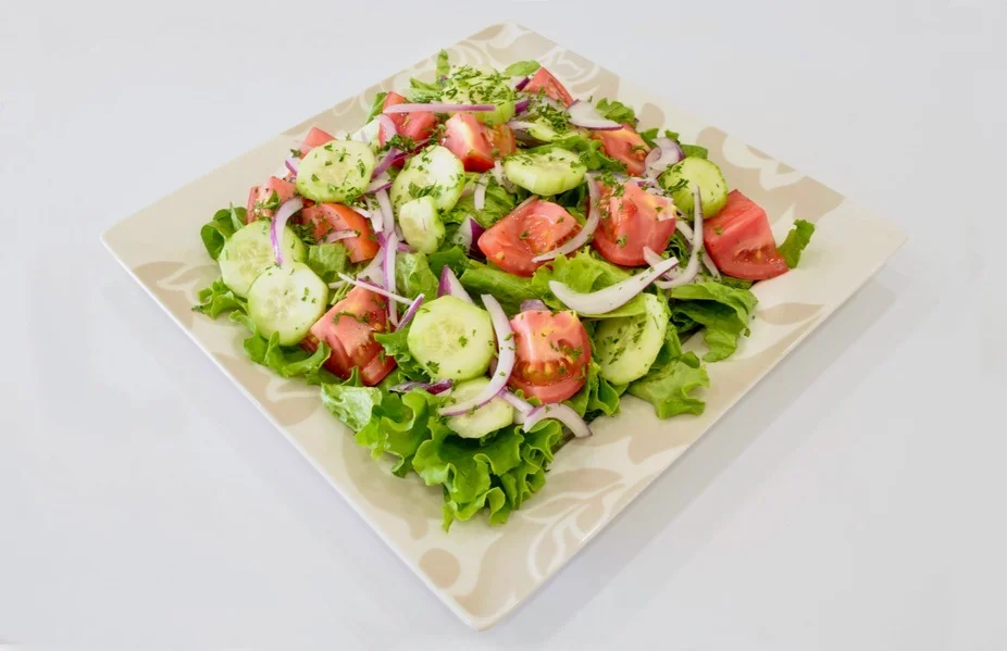 A fresh salad featuring layers of green lettuce, sliced tomatoes, cucumbers, and onions, garnished with herbs.