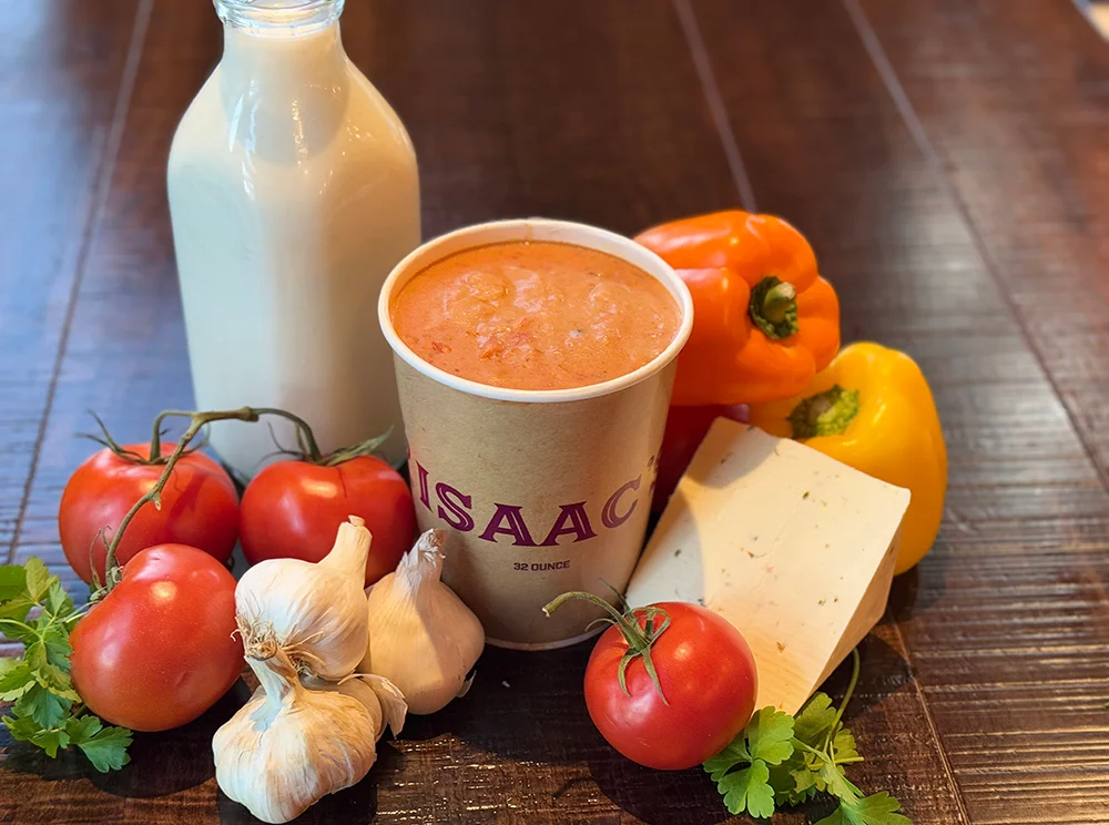 A quart of Isaac's Pepperjack Tomato Soup surrounded by fresh tomatoes, garlic, pepperjack cheese, yellow and orange bell peppers and fresh cream.