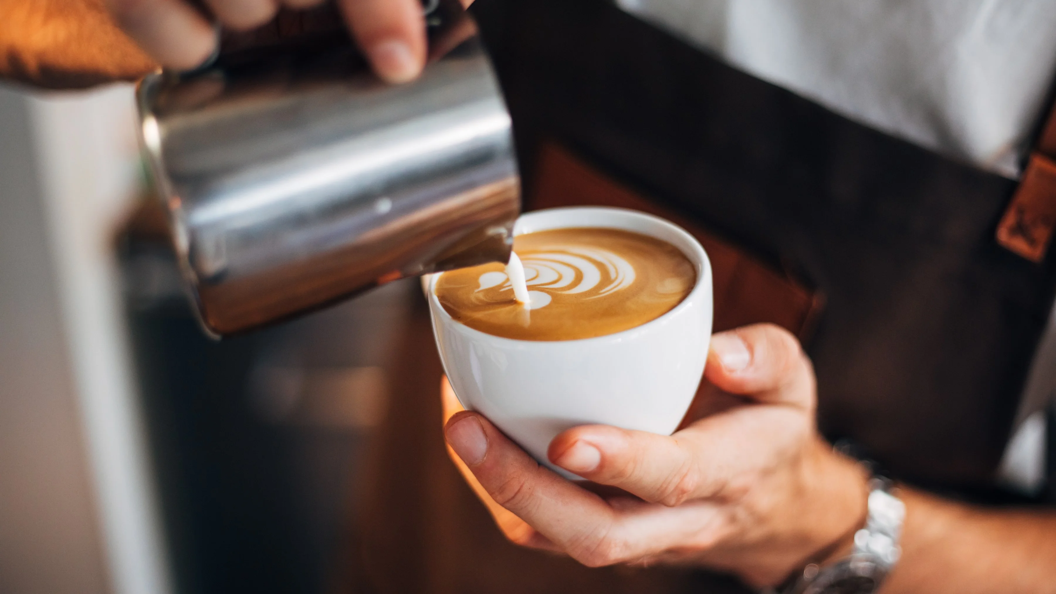 Barista pouring latte art into a white cup
