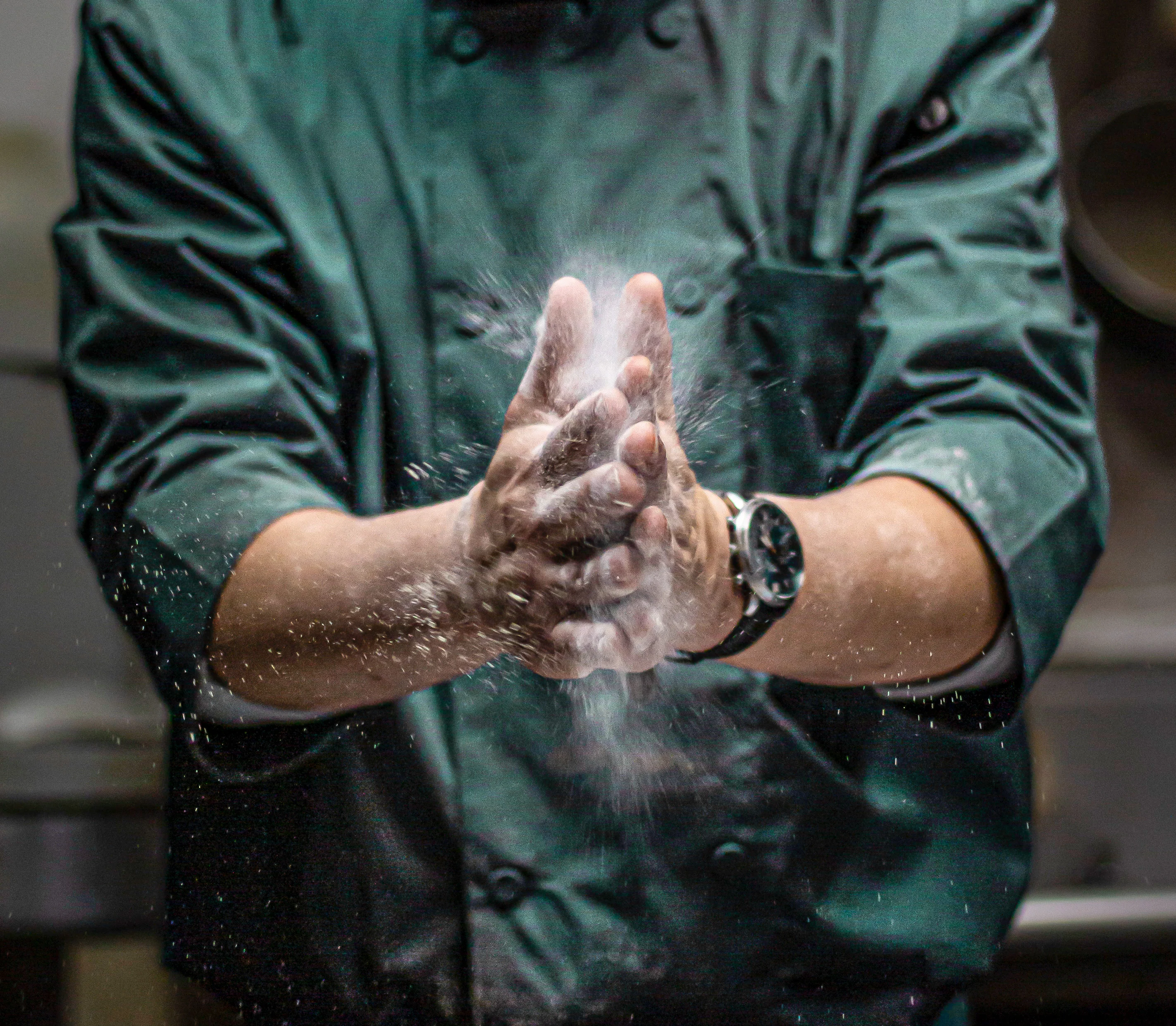 A chef's hands are seen dusting flour, showcasing the preparation process in a kitchen environment.