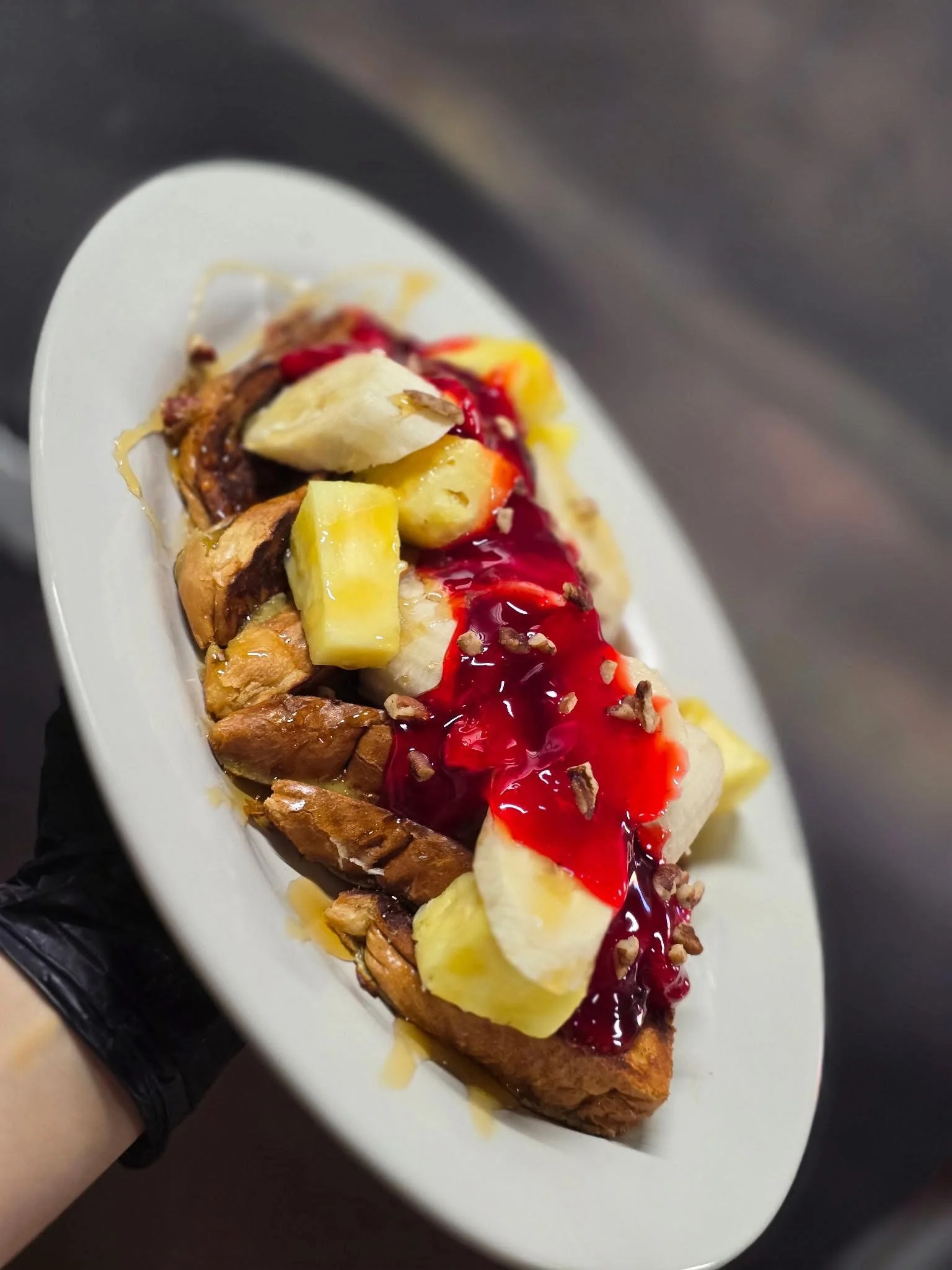 A plate of pastry topped with banana and pineapple chunks, drizzled with fruit sauce and sprinkled with pecans.