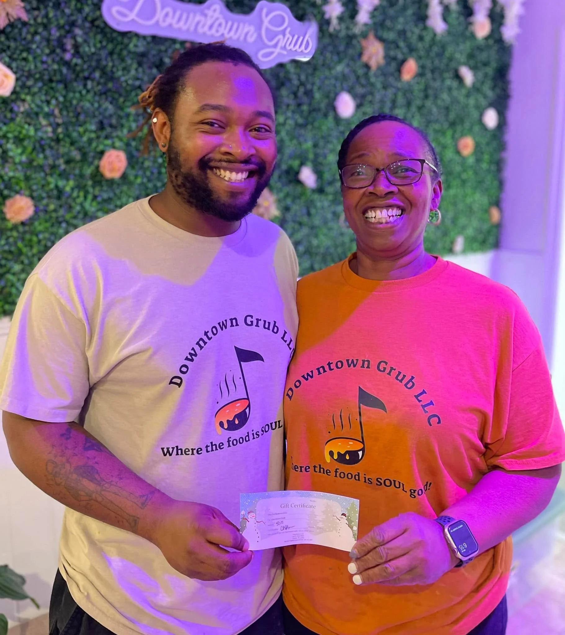 Two smiling individuals holding a gift certificate at Downtown Grub restaurant