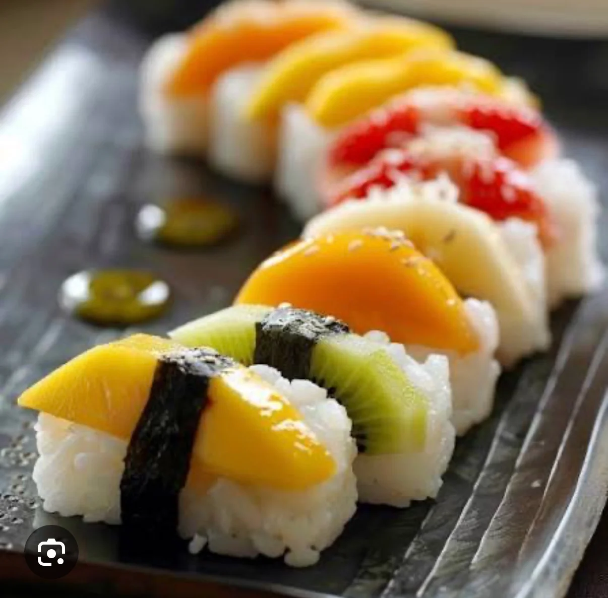 Colorful fruit sushi on a black plate