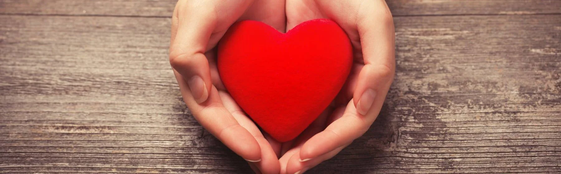 Hands holding a red heart on a wooden table