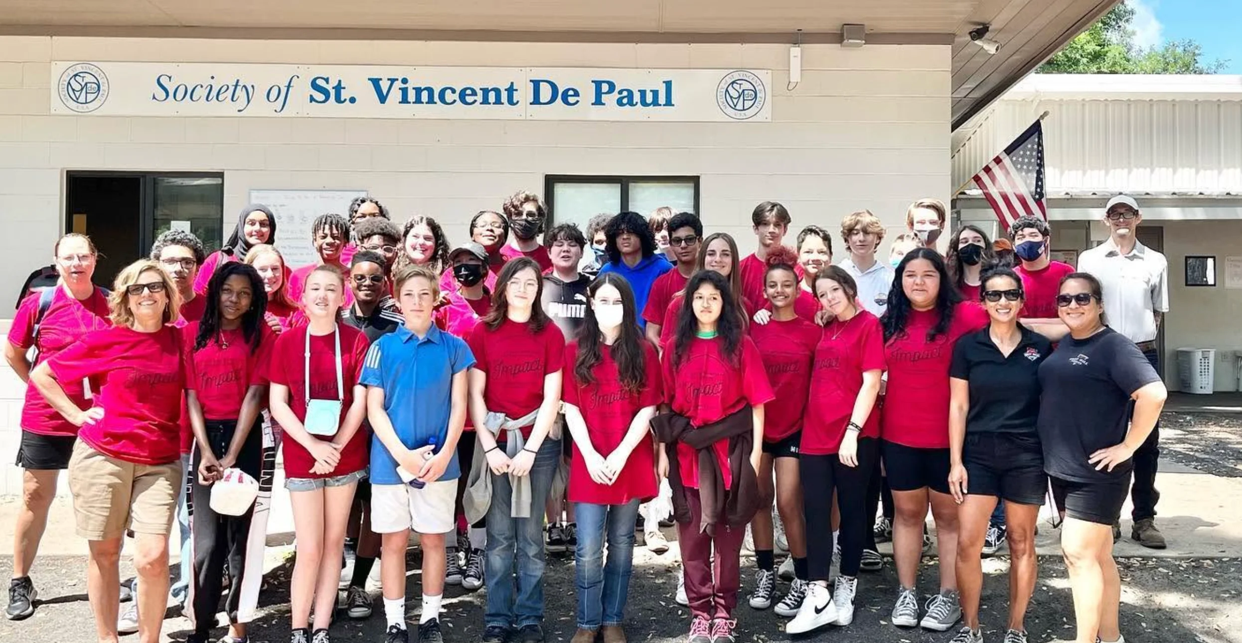 Large volunteer group posing outside a community center with an American flag