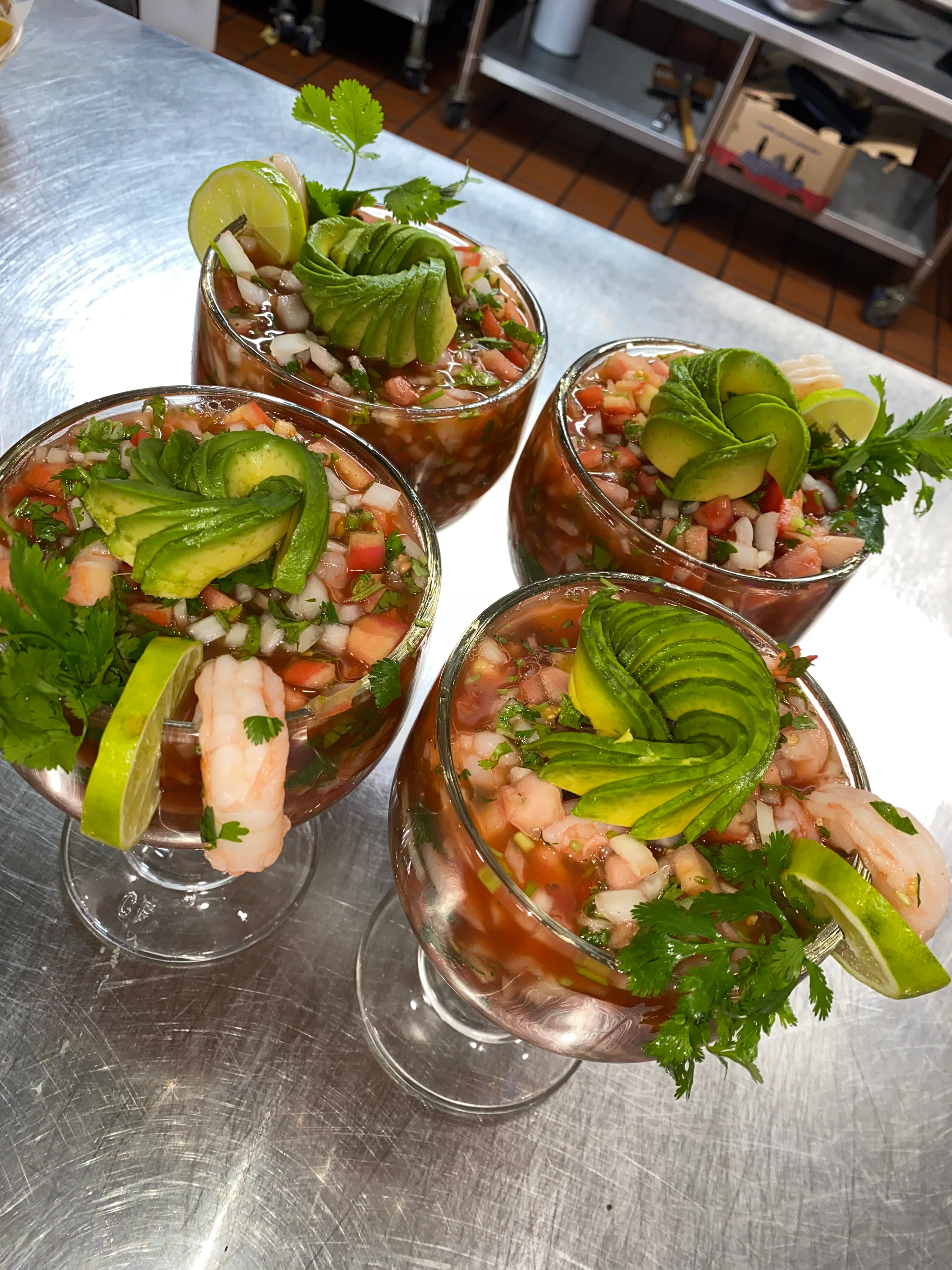 Four glasses of seafood cocktail, beautifully garnished with avocado, lime, and cilantro over diced tomatoes and onions.