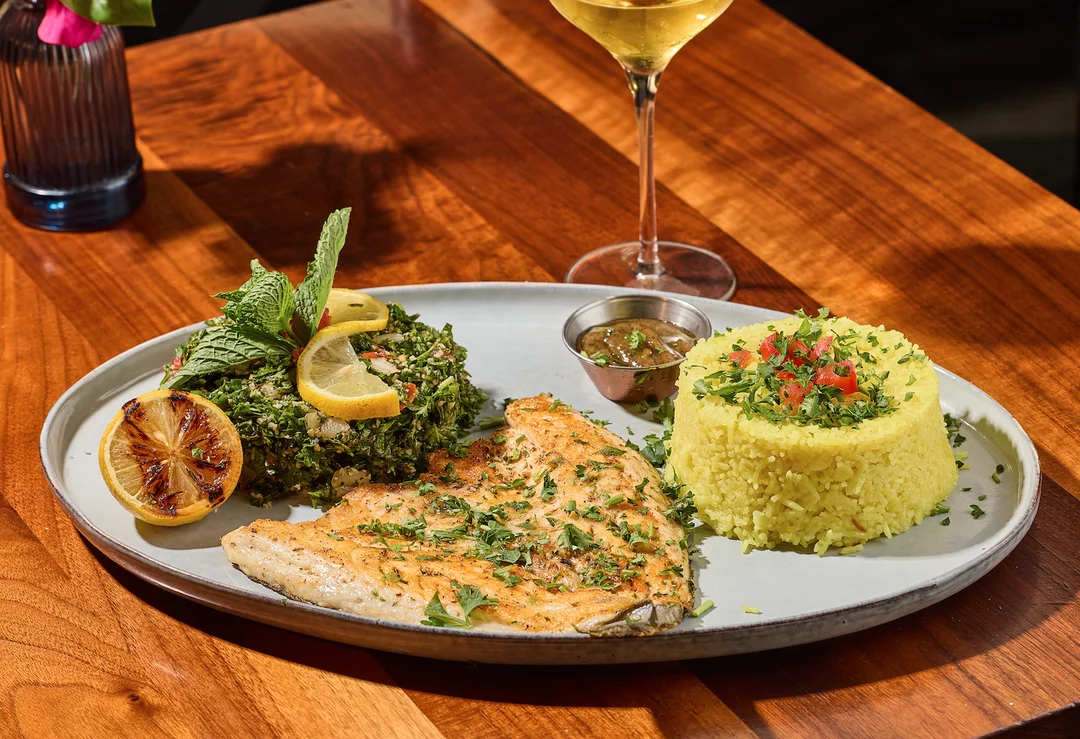 Grilled fish with rice, salad, and a glass of wine on a wooden table.