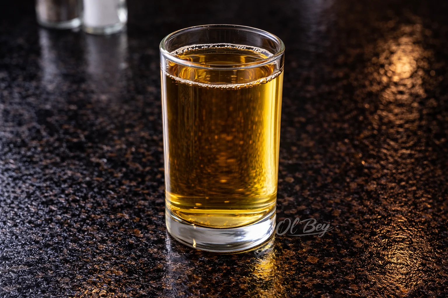 A clear glass filled with a light amber liquid, placed on a polished dark surface.