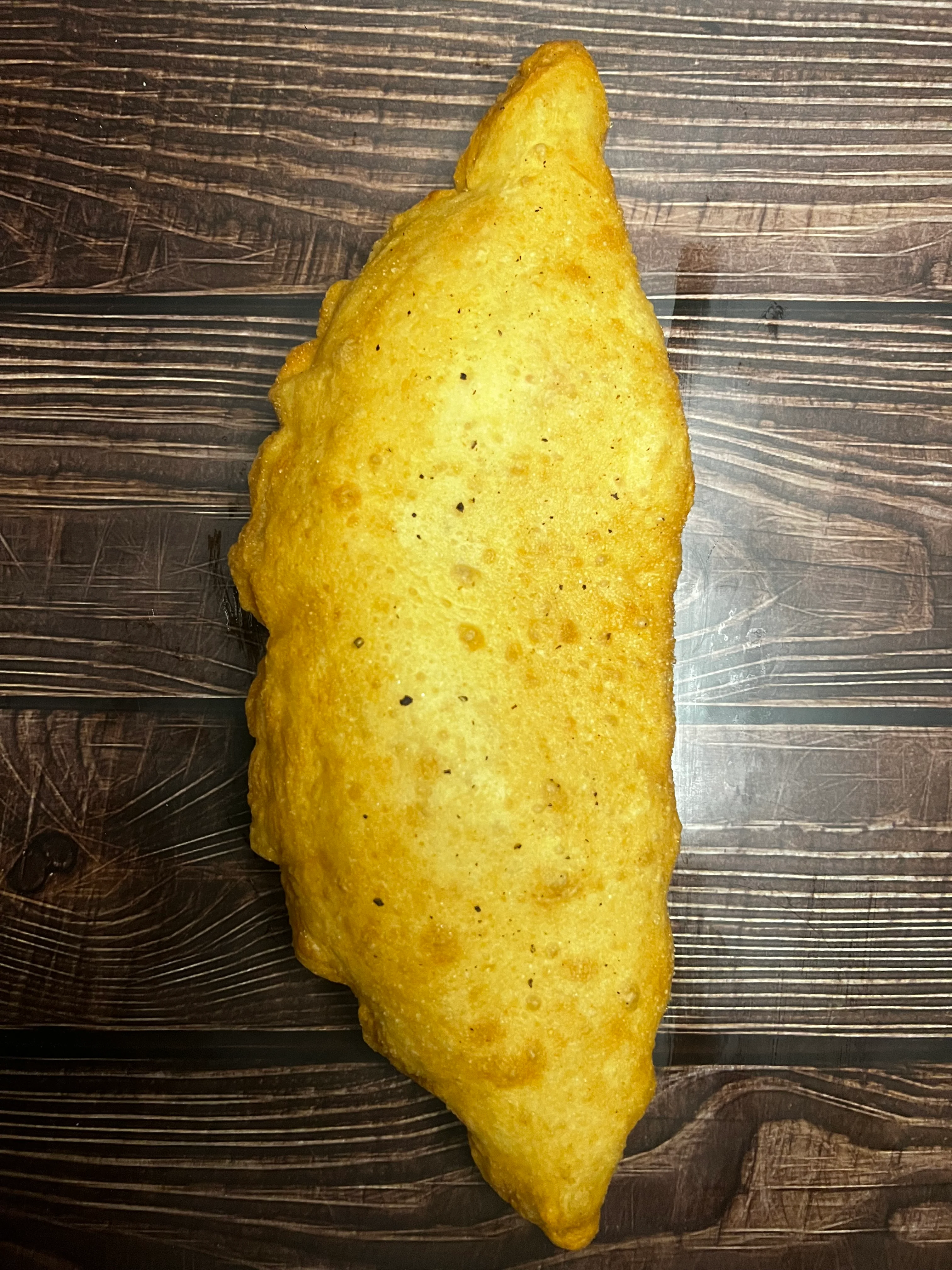 Golden fried Jamaican patty on a wooden table