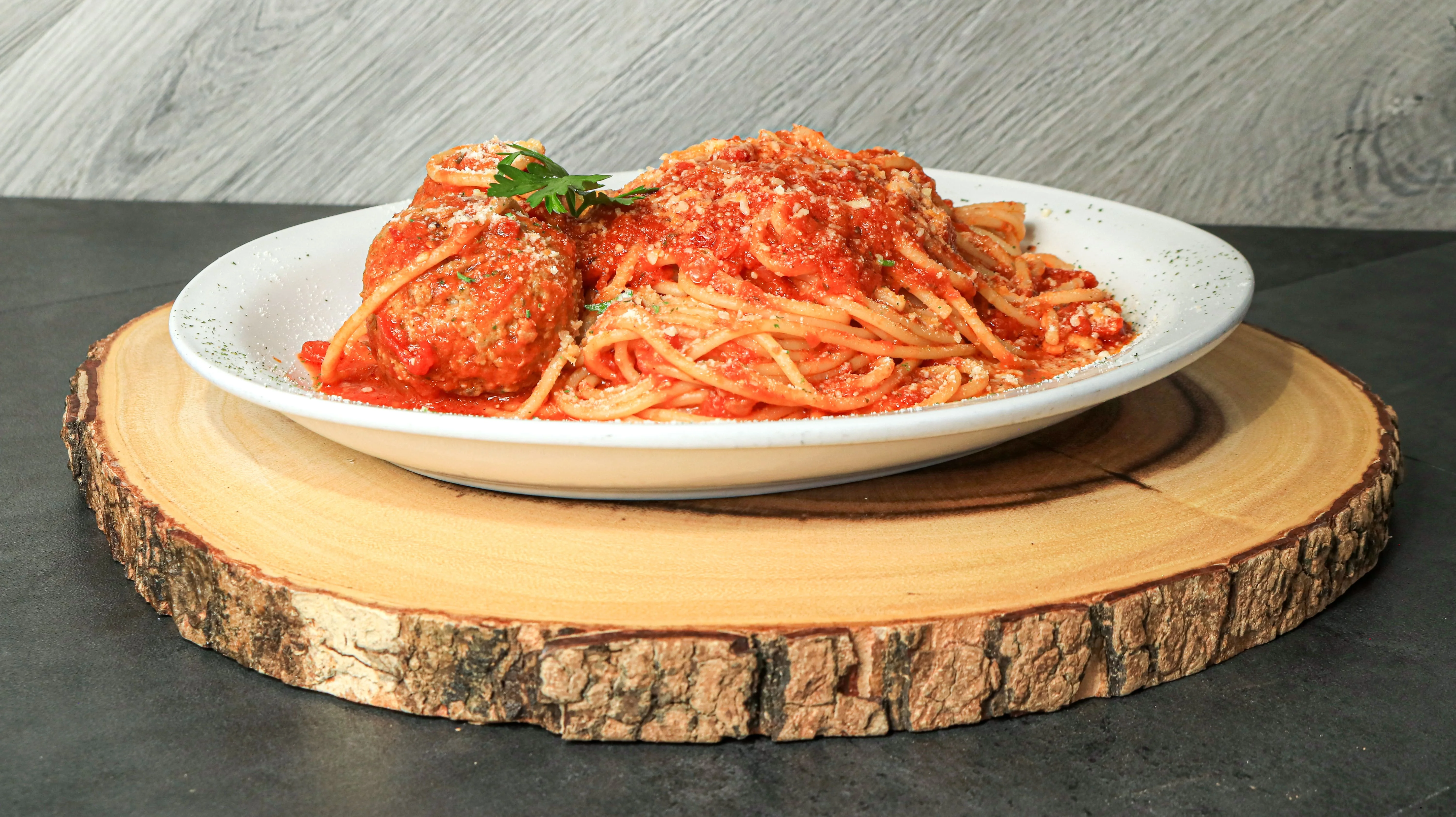 A serving of spaghetti topped with meatballs and marinara sauce, garnished with parsley, served on a wooden plate.