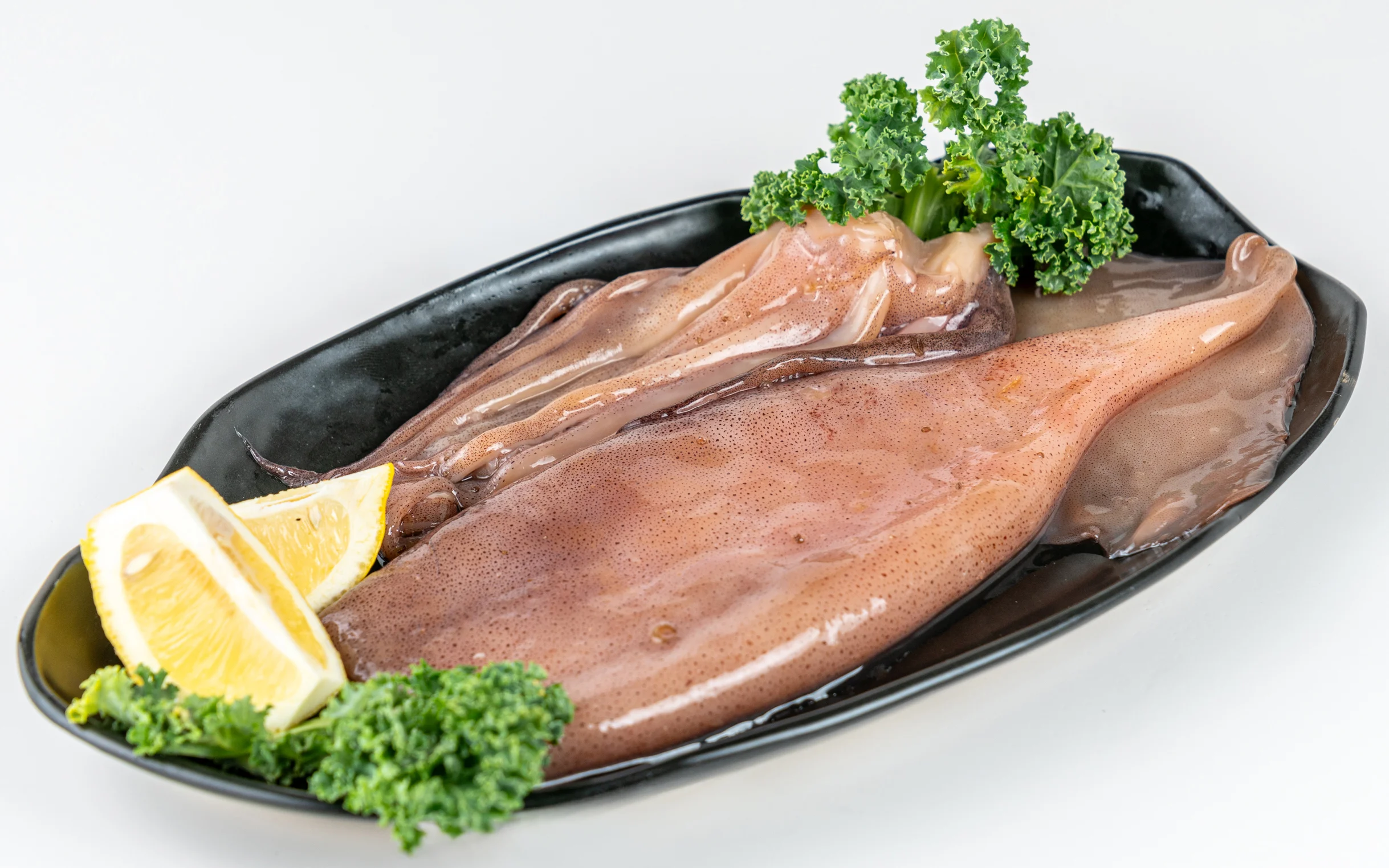 Fresh squid served on a black plate with lemon and greens