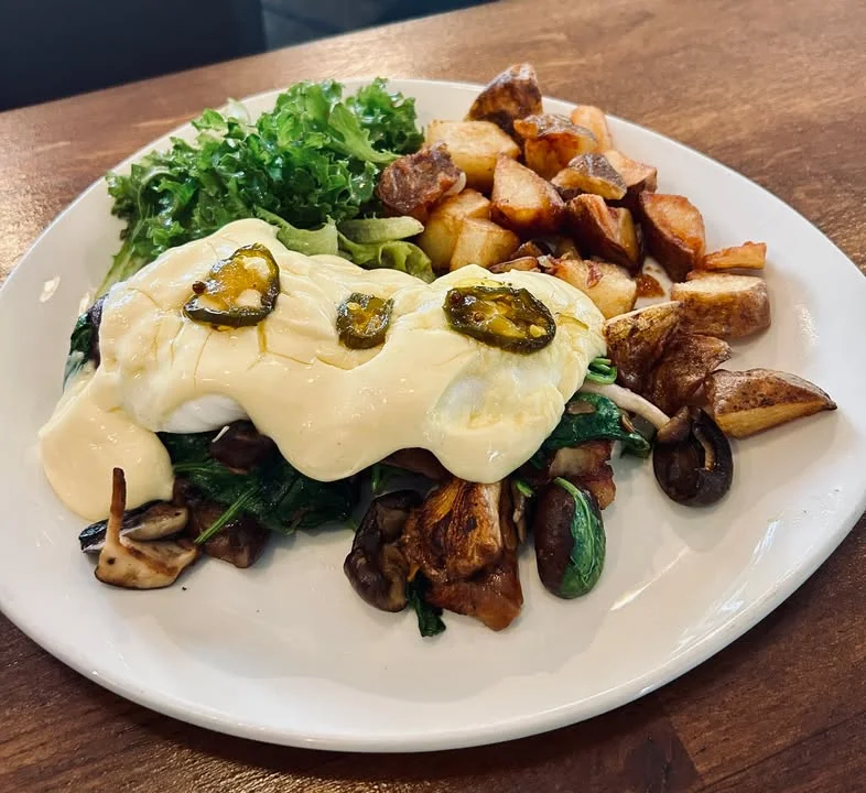 A vibrant plate featuring poached eggs with spinach, jalapeños, and creamy sauce, accompanied by a side of potatoes and fresh greens.