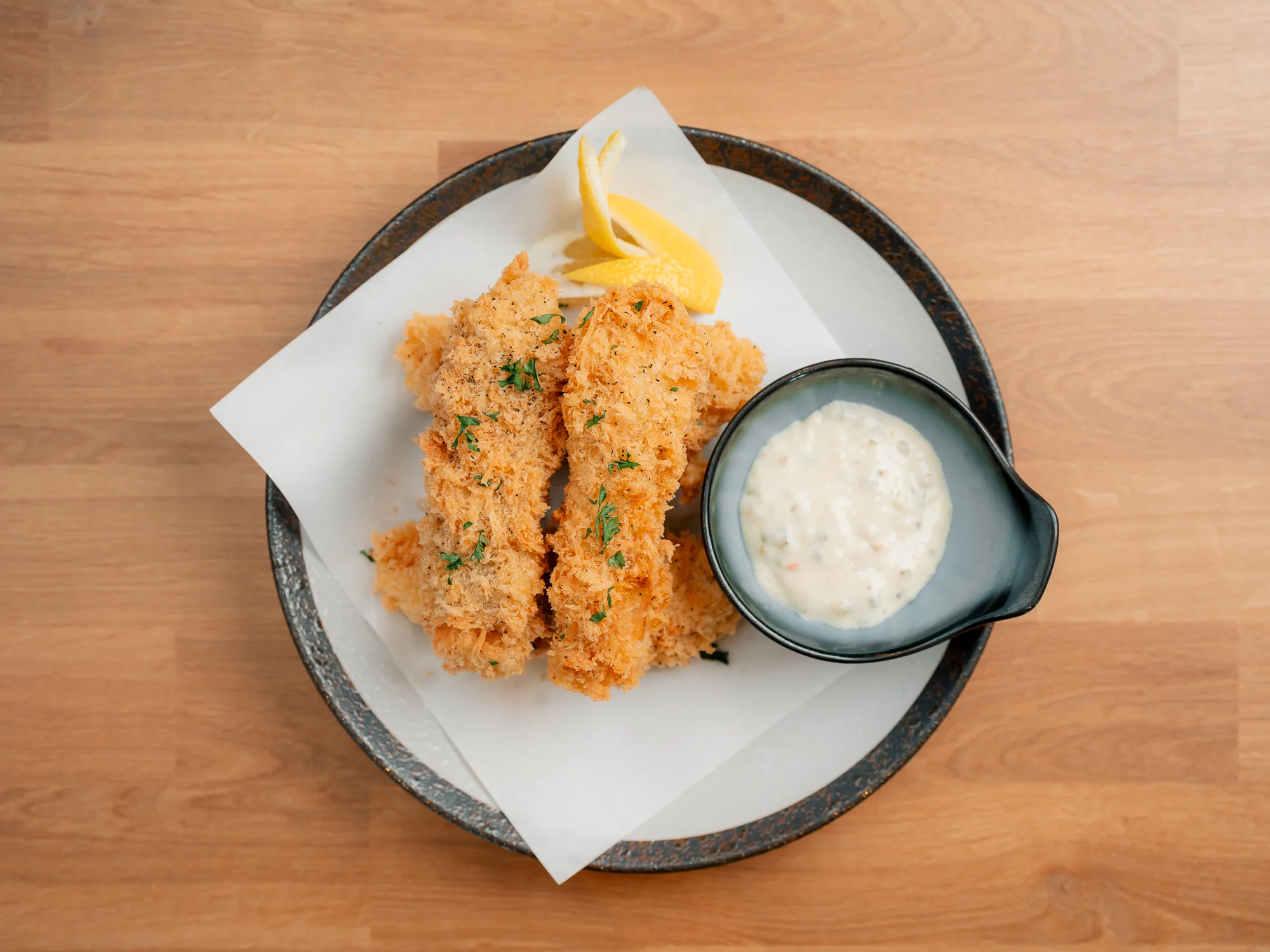 Two crispy fried fish fillets served with a side of creamy dipping sauce and a wedge of lemon.