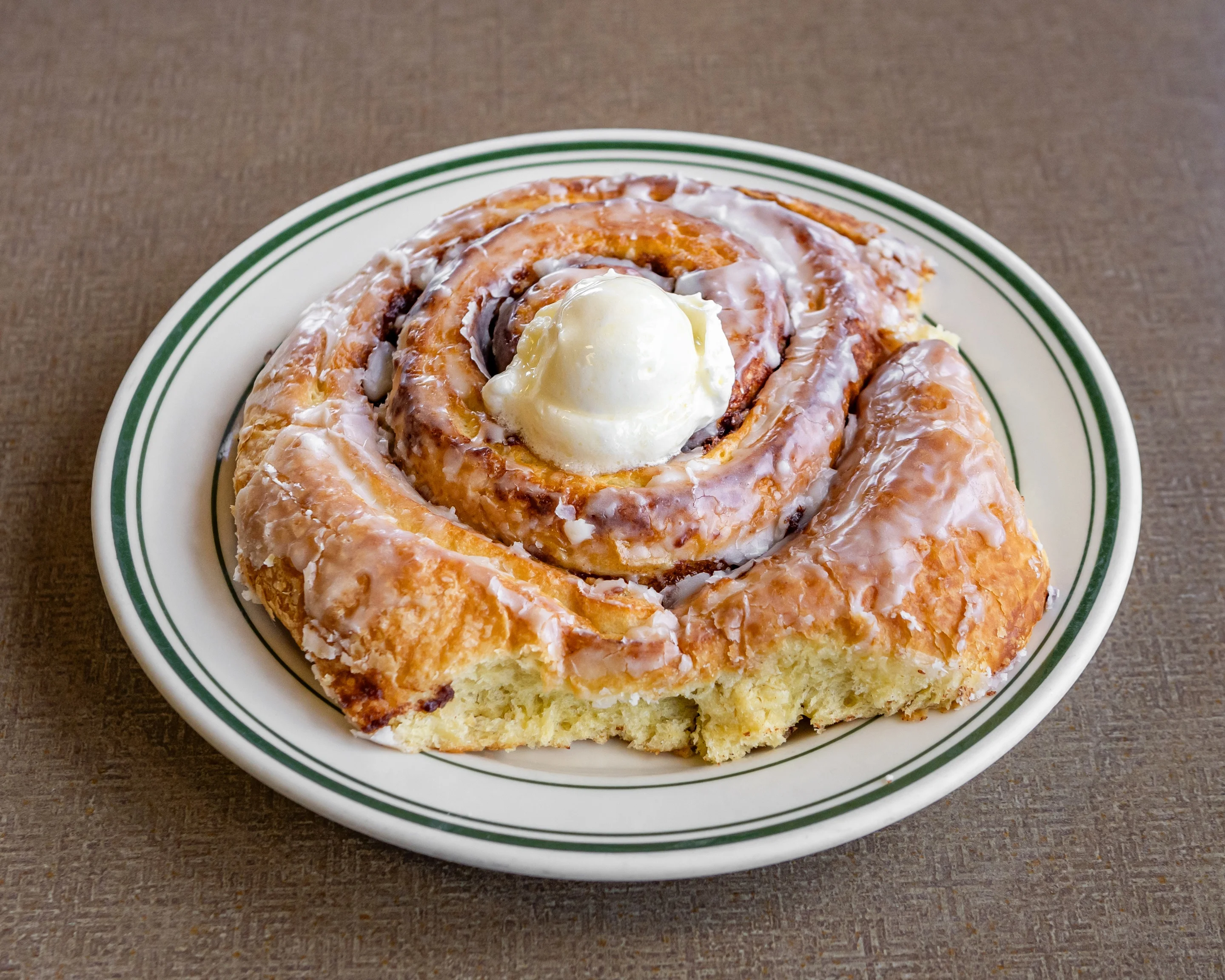 A large cinnamon roll drizzled with icing and topped with a scoop of ice cream on a white plate.