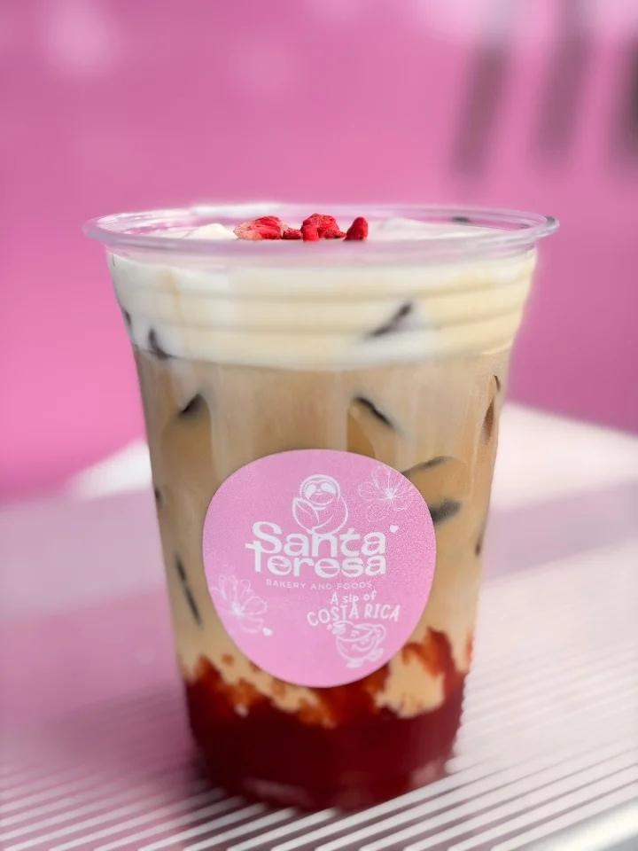 A layered iced drink with a mix of coffee and a vibrant red base, topped with a creamy layer and garnished with dried fruit.