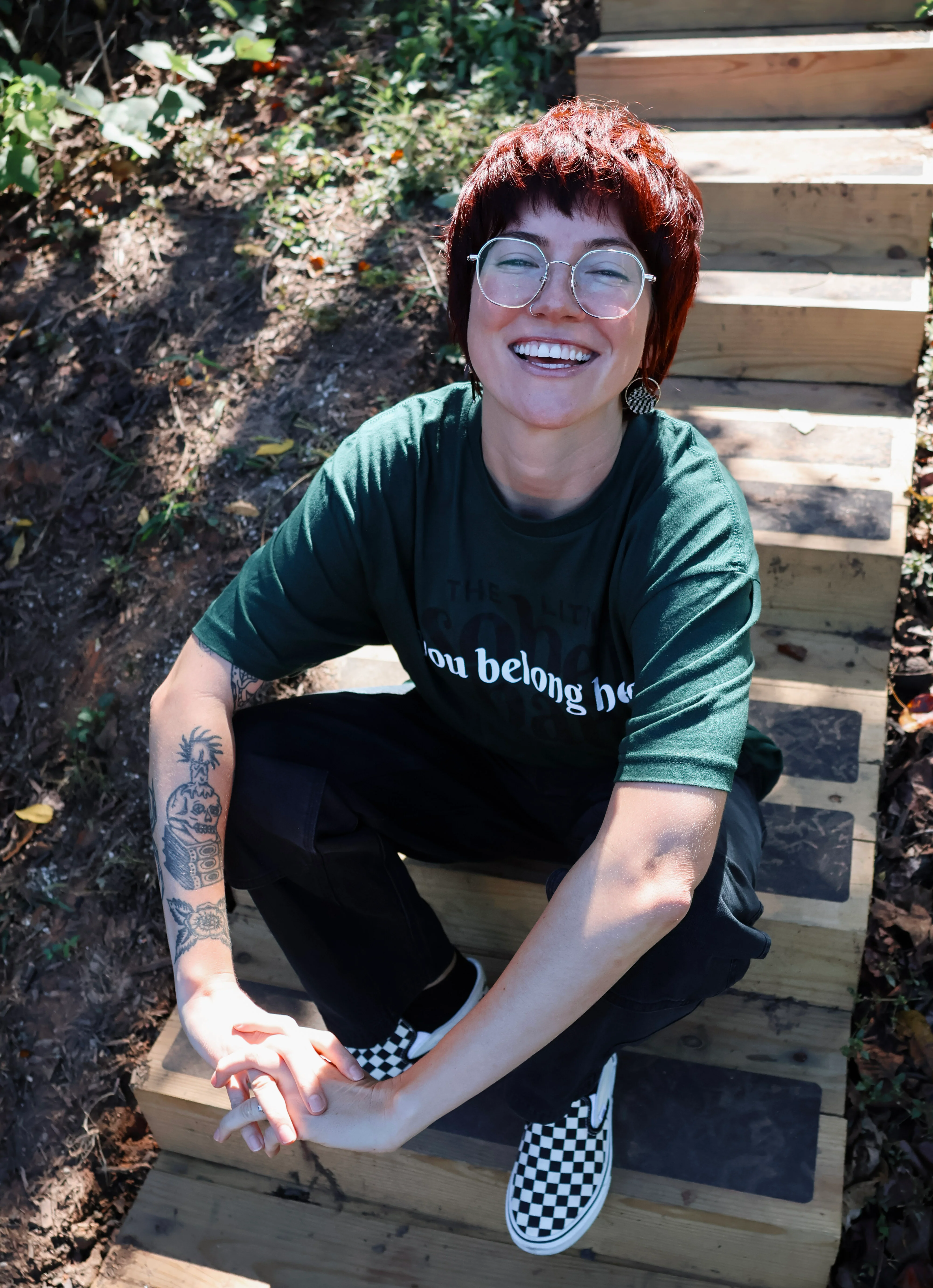 Smiling person wearing glasses outdoors beside a garden bench