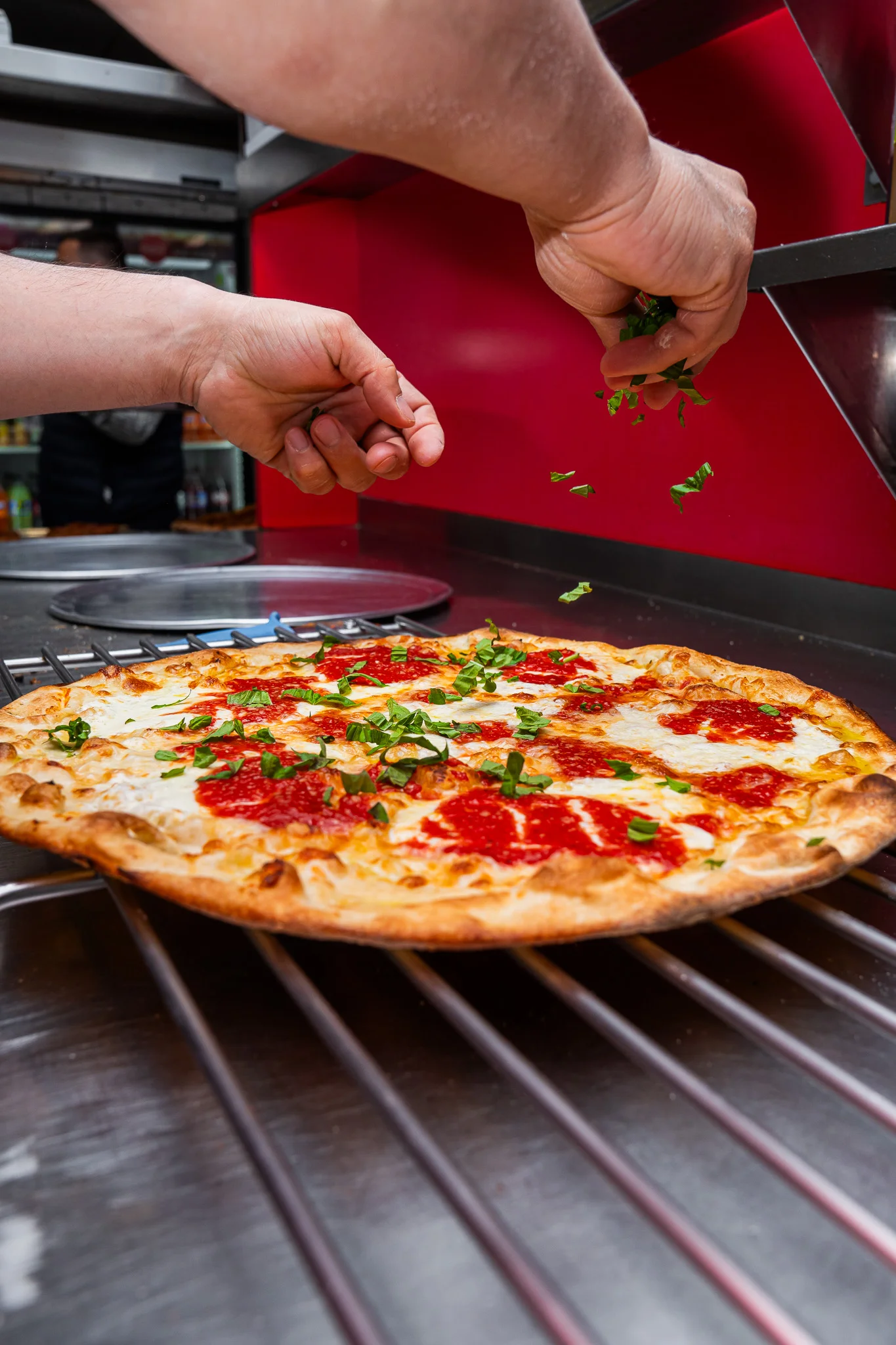 Fresh Margherita pizza being garnished with herbs