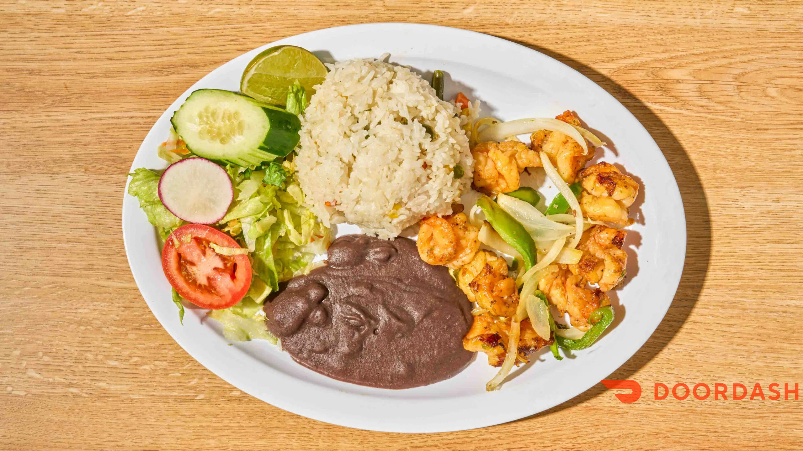 Plate of shrimp with rice, beans, and fresh vegetables on a wooden table.