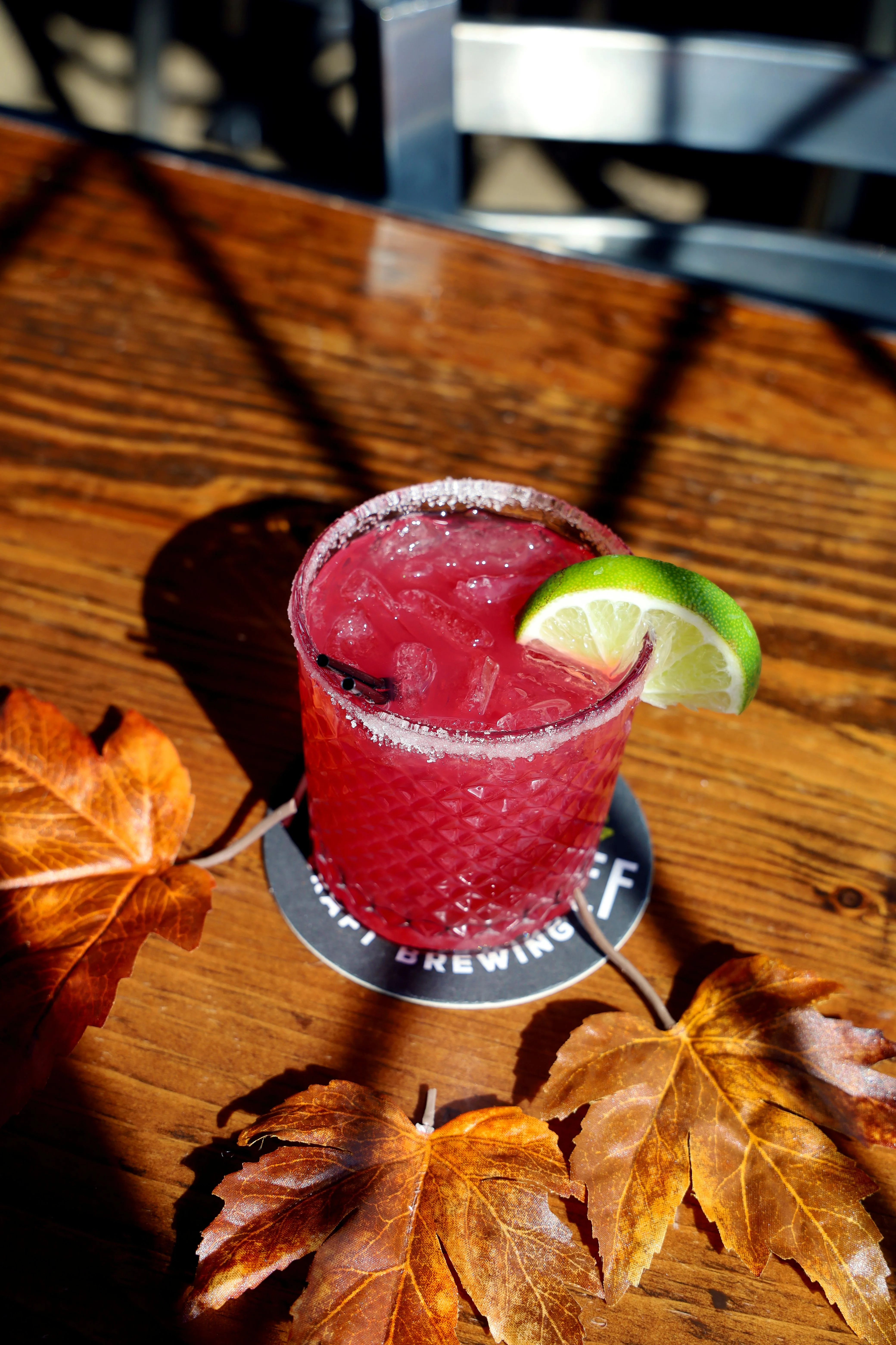 Close-up of a vibrant red cocktail with lime garnish on a wooden bar
