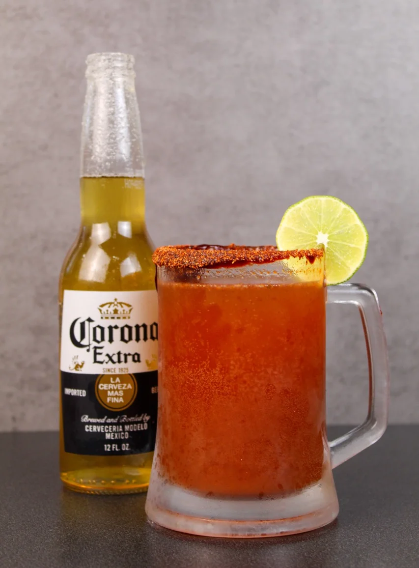A clear glass of dark beer sitting on a wooden table, with a soft-focus background featuring ambient lighting.