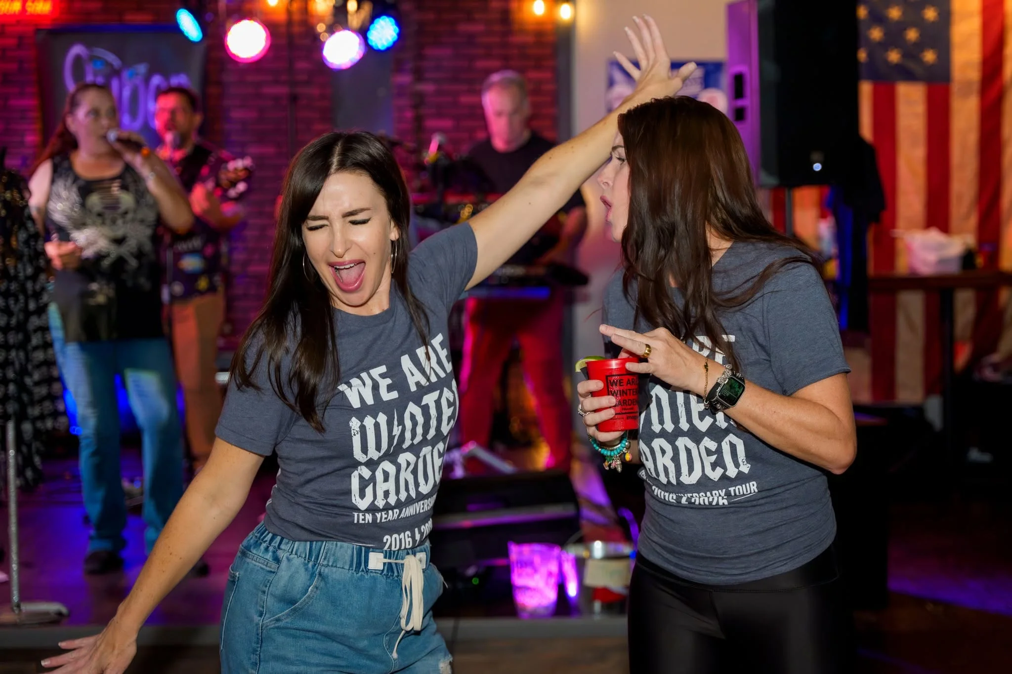 Two women dancing joyfully at a lively bar with a band in the background