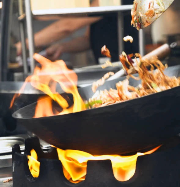 Chef stir-frying vegetables in a wok over an open flame