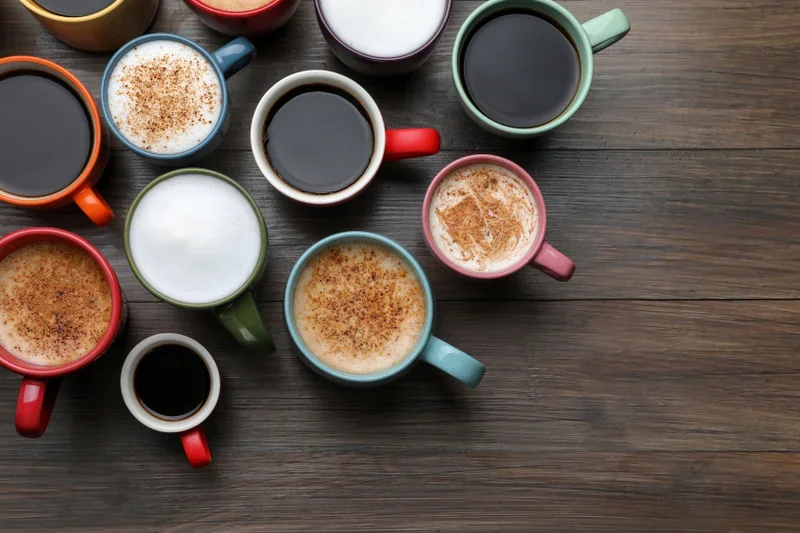 A collection of colorful mugs filled with various types of coffee, arranged on a wooden surface.