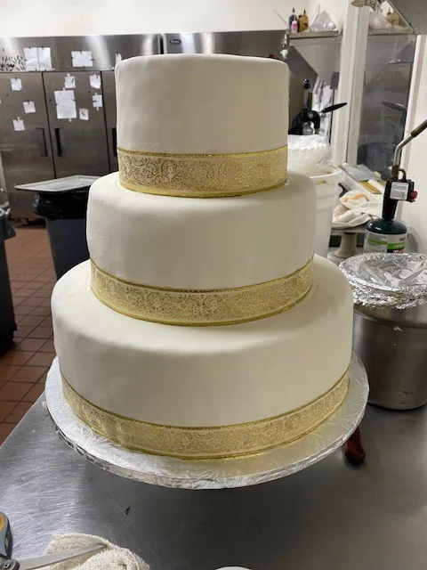 Three-tier white fondant cake with gold ribbon from The Kosher Pastry Oven
