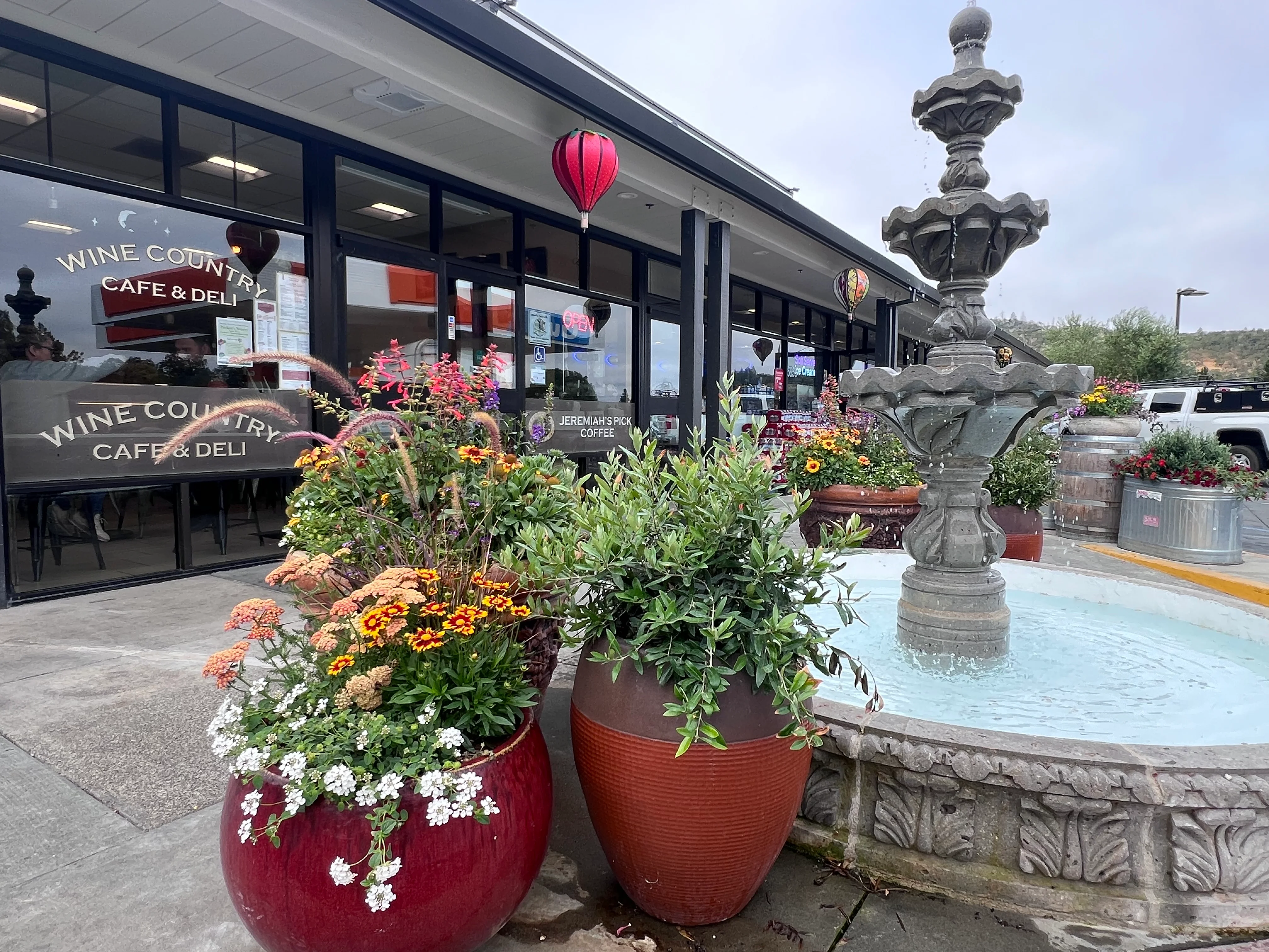 large red planters full of flowers next to a water fountain in front of Wine Country Cafe & Deli