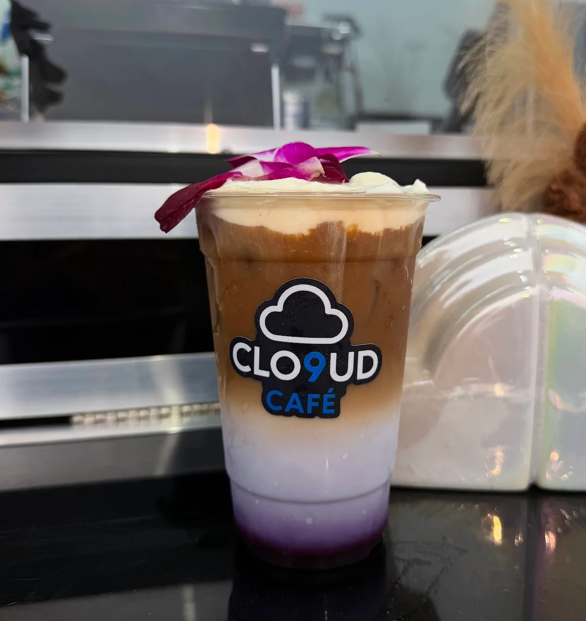 Two refreshing drinks with vibrant colors, each served in clear cups featuring a logo. The drinks are topped with fruit pieces and served with straws.