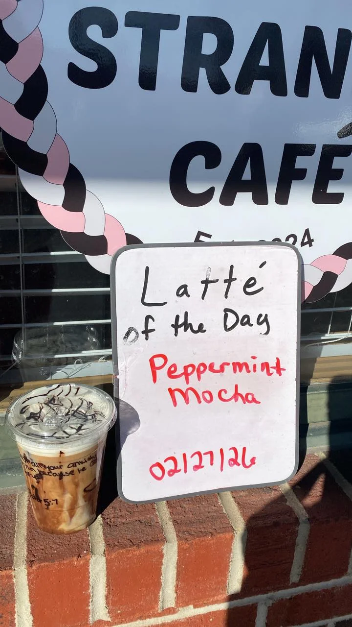 A sign outside a cafe displaying the latte of the day, which is Peppermint Mocha, next to a prepared drink in a clear cup.