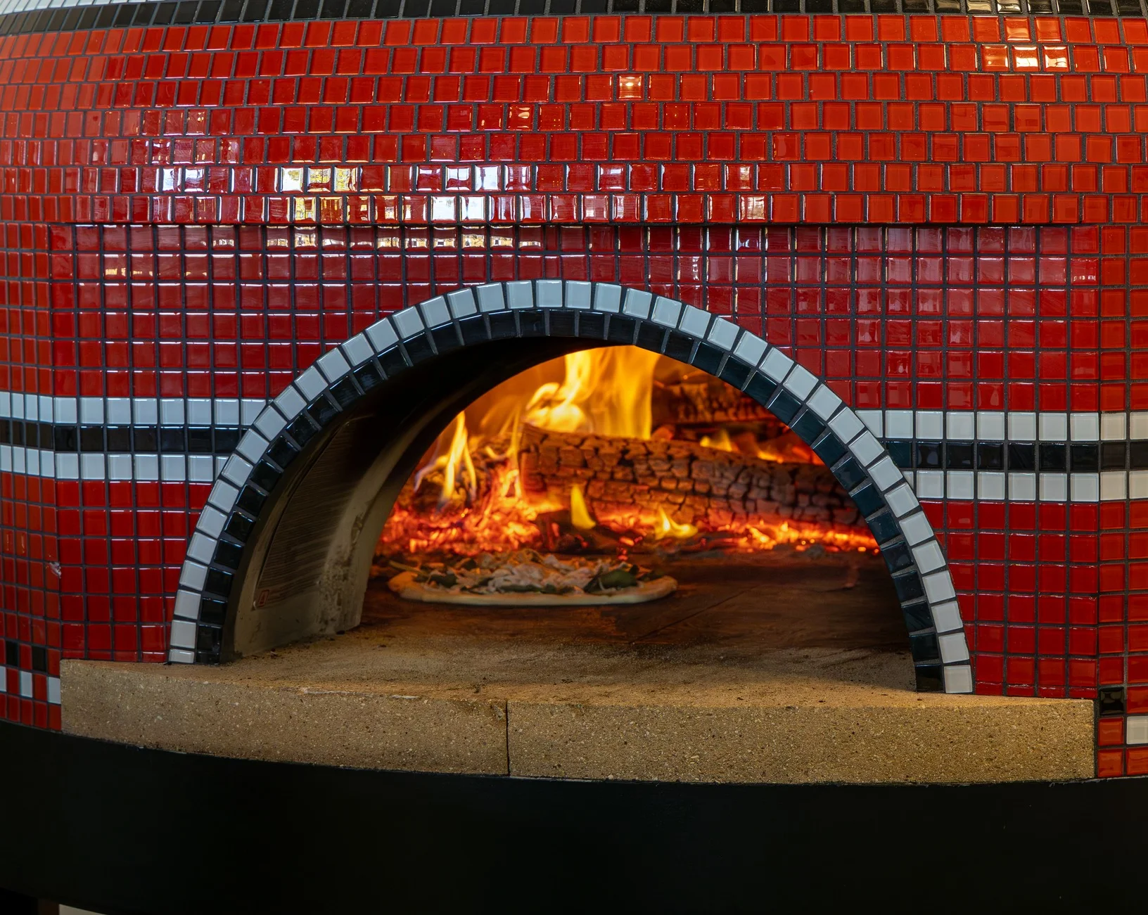 A circular logo featuring the name 'Tin Roof Kitchen Co.' with icons representing pizza and burgers. The design includes a chimney and a red and black color scheme.
