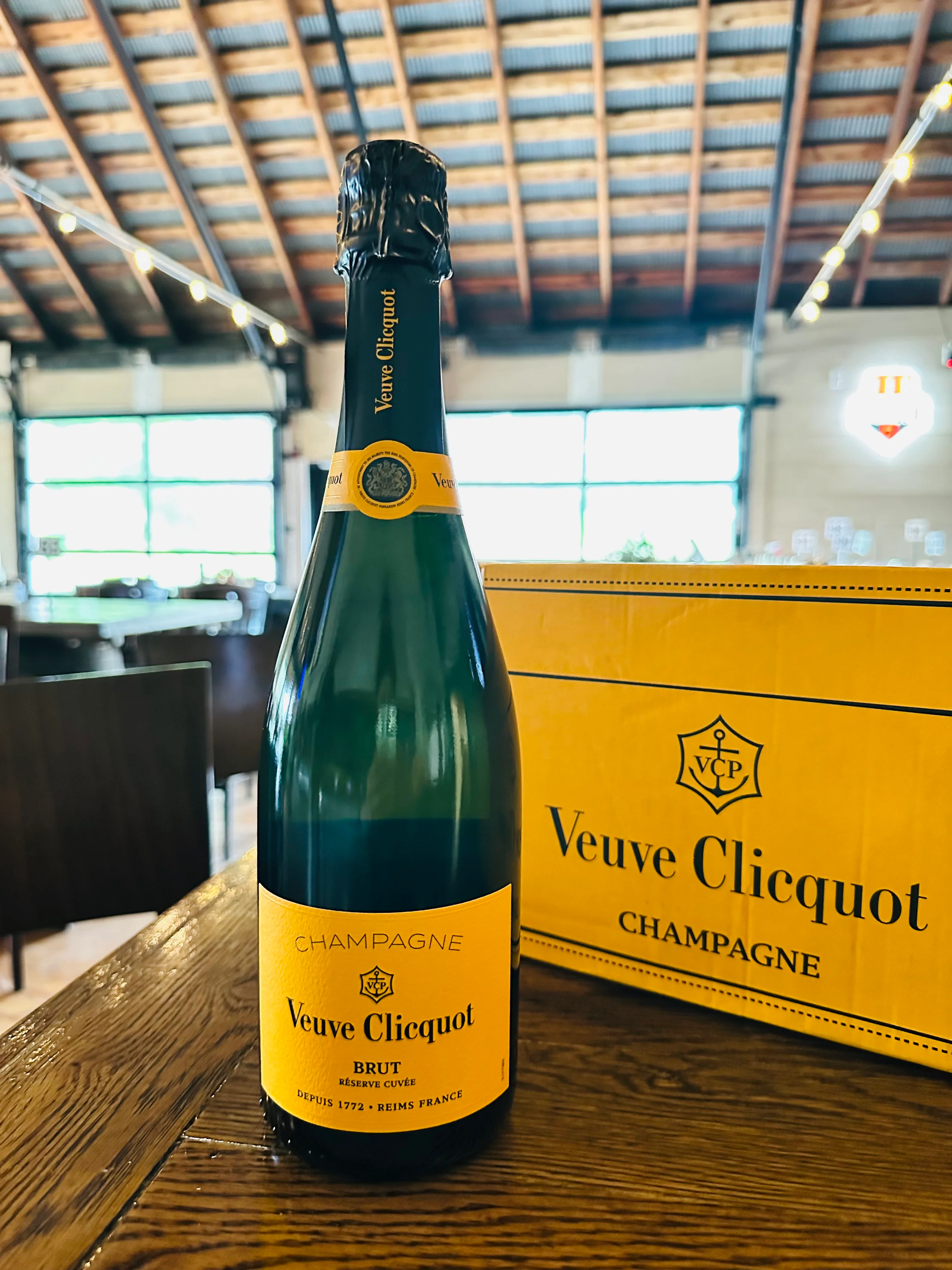 A bottle of champagne from Veuve Clicquot, displayed on a wooden table with the brand's box in the background.