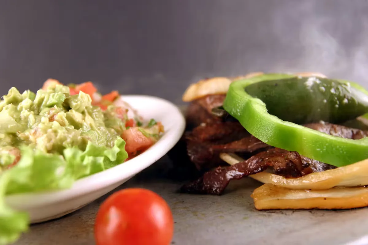 Fresh guacamole next to beef fajitas with a green pepper