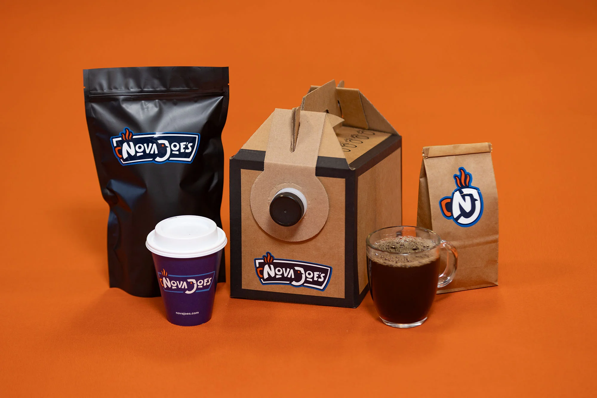 A variety of coffee products including two bags of beans, a cardboard carafe and a cup of coffee.