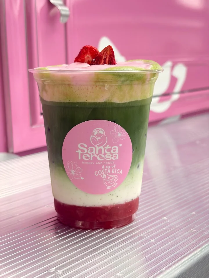 A colorful drink with matcha, creamy layers, and a red berry base, garnished with a slice of strawberry on top.