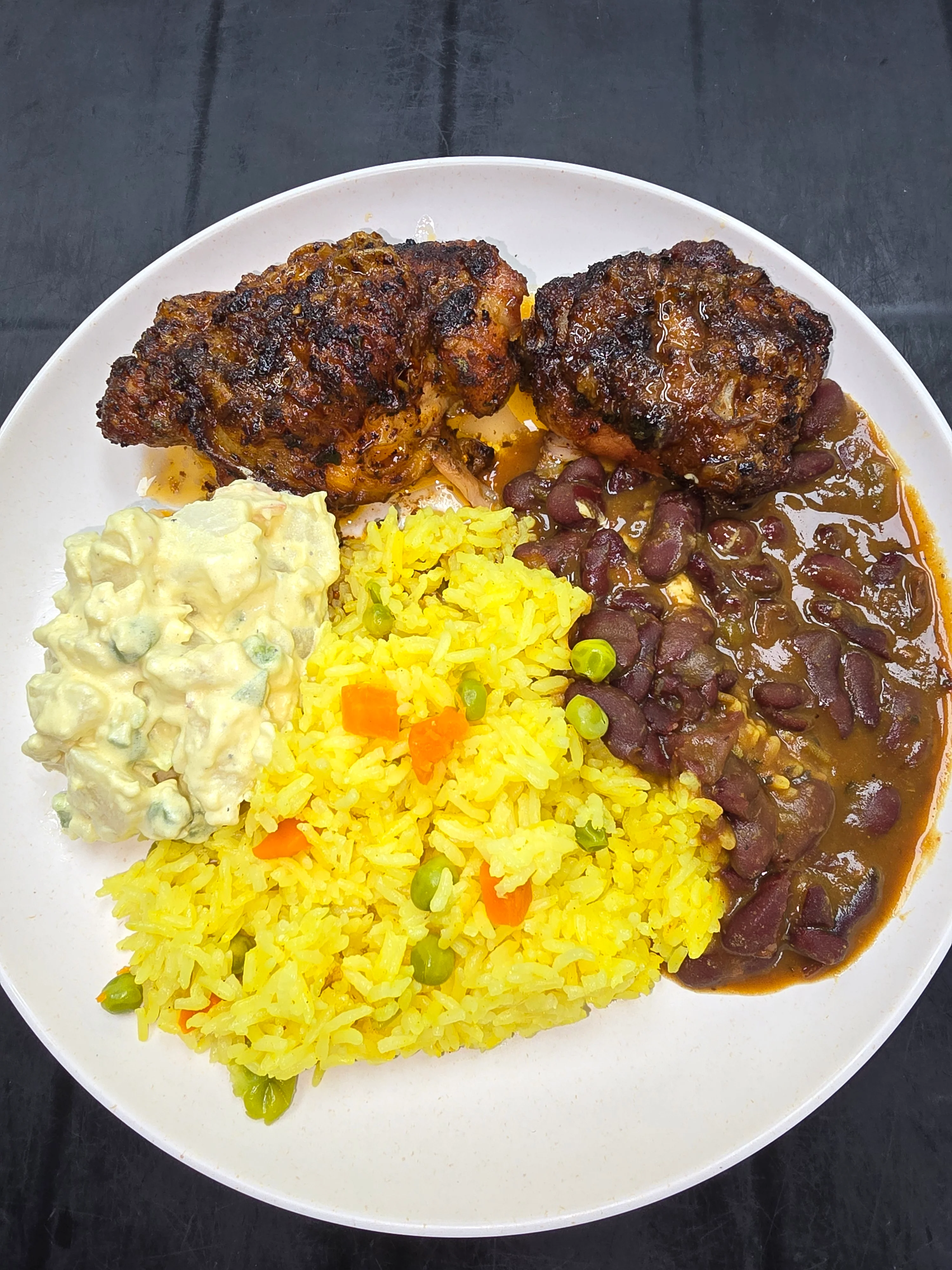 Plate of seasoned chicken, yellow rice, beans, and potato salad.