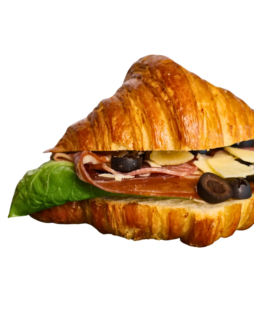 A croissant sandwich filled with ham, olives, and cheese, garnished with fresh spinach.