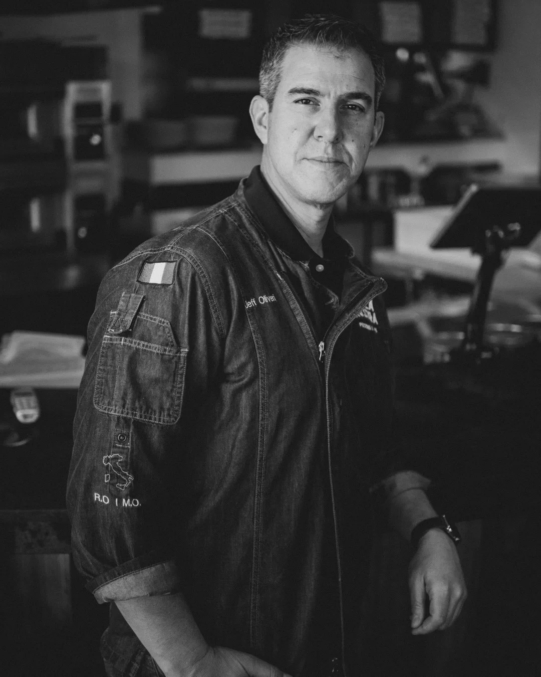 A man in a denim jacket stands confidently in a restaurant setting.