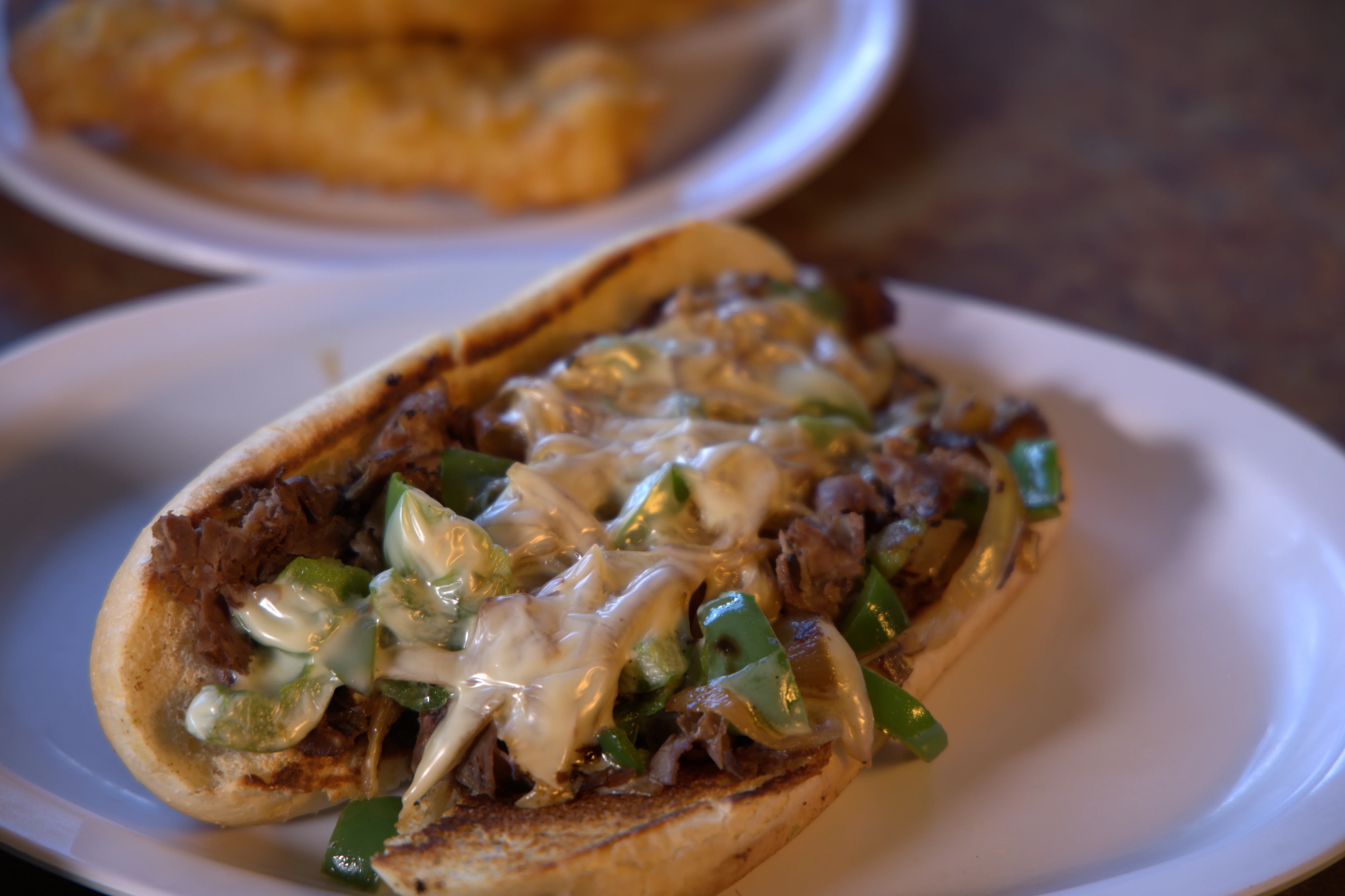 A close-up of a meat-filled roll topped with green peppers and melted cheese, placed on a white plate.