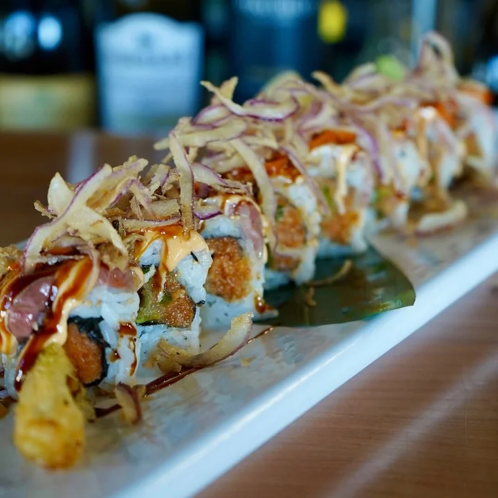 A plate of sushi rolls garnished with fried onions, drizzled with sauces, showcasing a variety of ingredients.